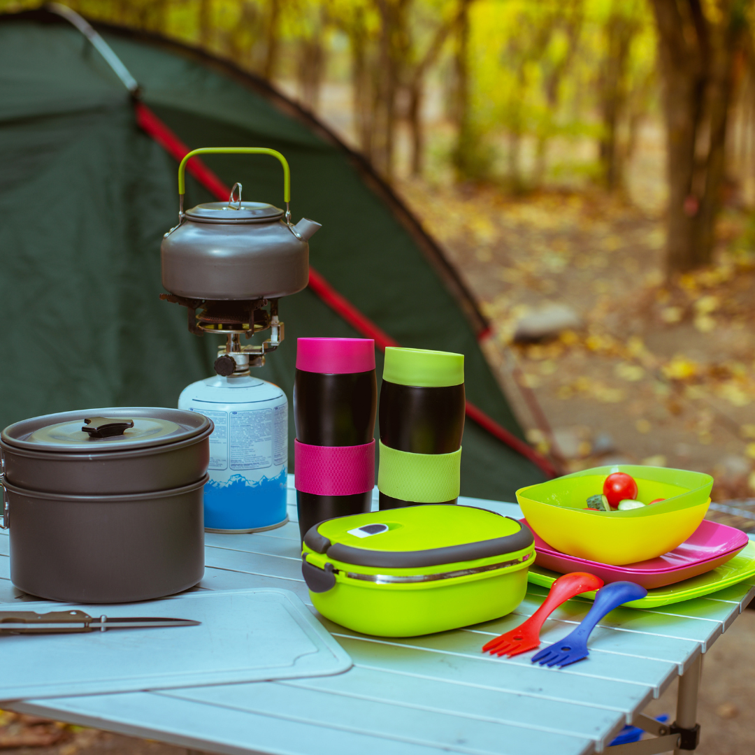 Portable camping stove with pots, utensils, and colorful mess kit for outdoor cooking and survival.