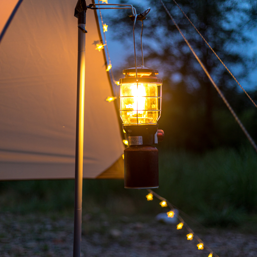 Camping lantern providing outdoor lighting under a tent with string lights at dusk.