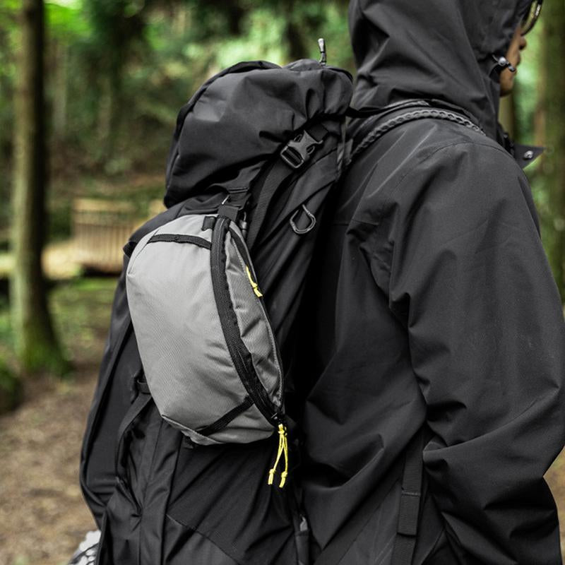 Person wearing a black jacket and carrying a gray backpack in a forest setting