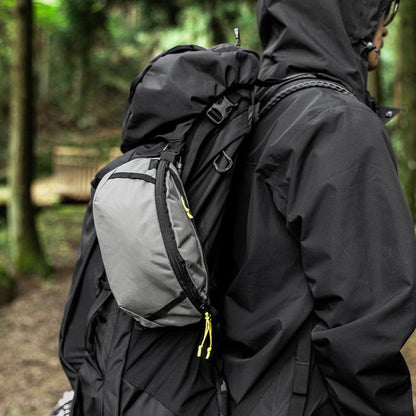 Person wearing a black jacket and carrying a gray backpack in a forest setting