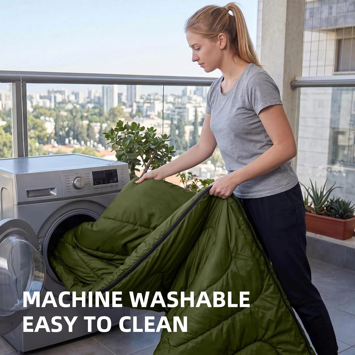 A woman on a balcony is holding an olive green puffer sleeping bag next to a washing machine, with text overlay that reads 'MACHINE WASHABLE EASY TO CLEAN'.