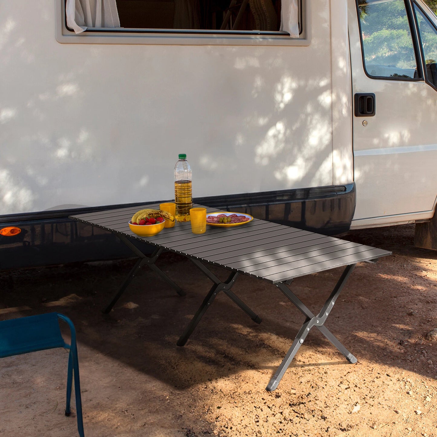 Portable folding table set up outdoors next to a white van with food and drinks on it.