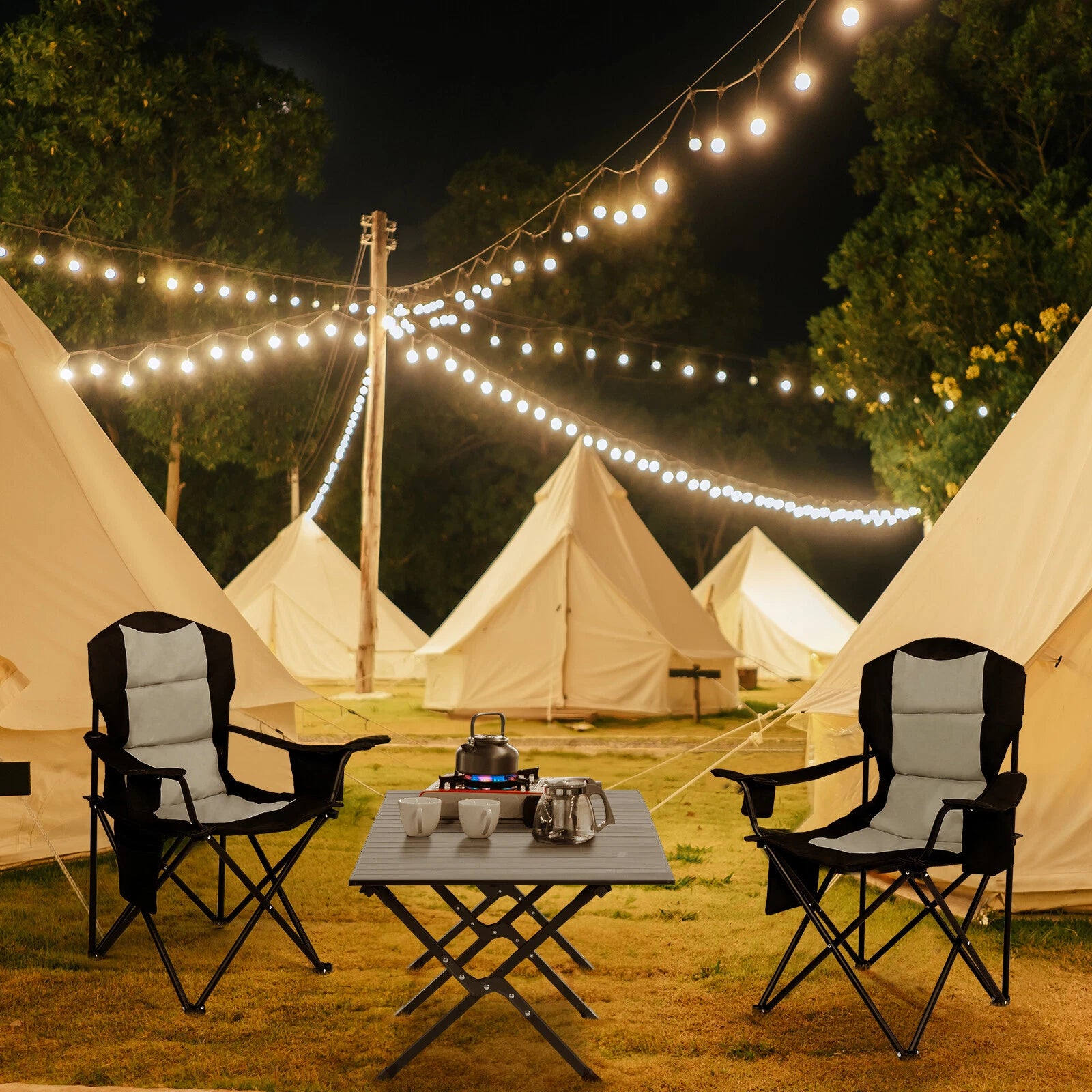 Camping scene with tents, chairs, and a small table under string lights at night.