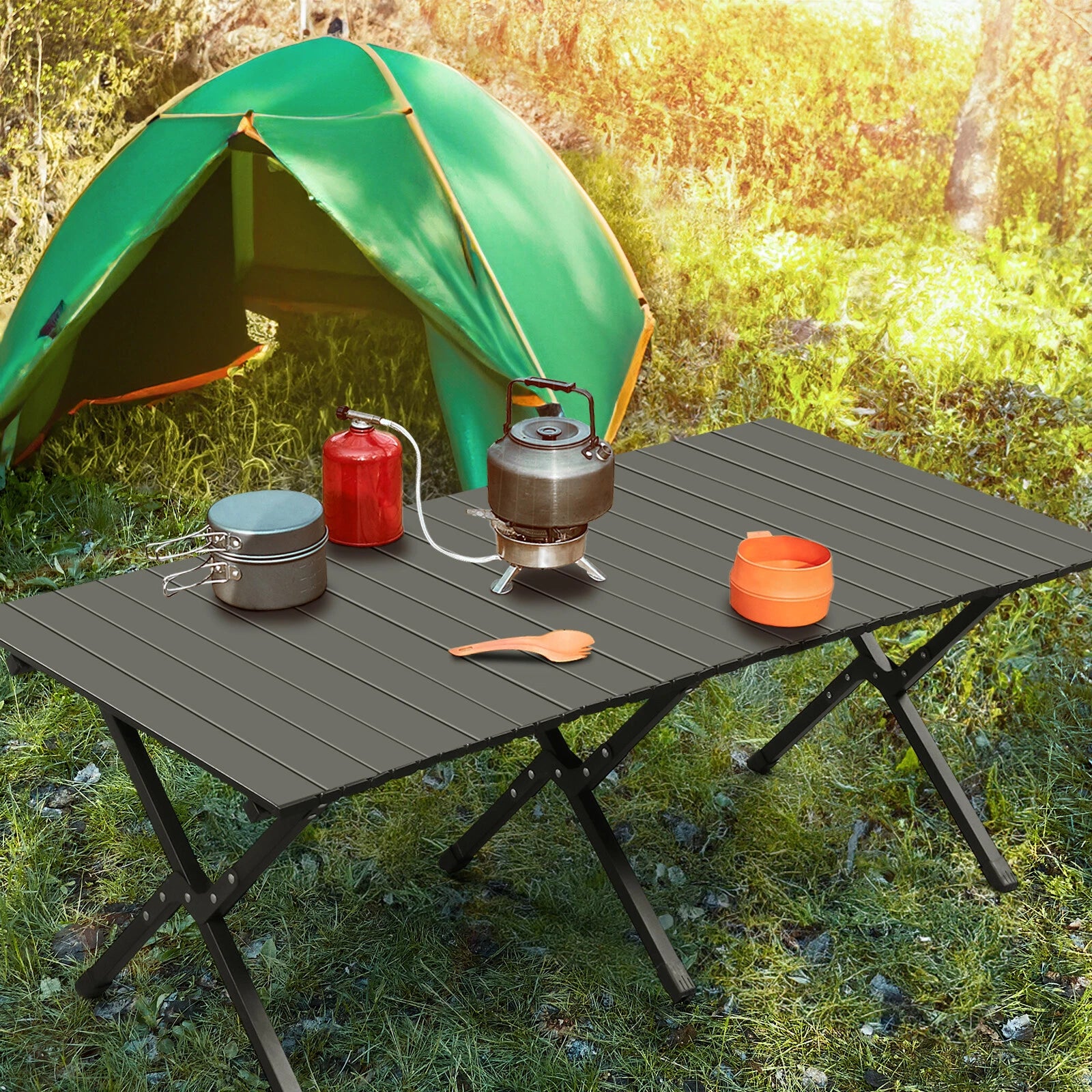 Camping setup with a green tent, gray folding table, and camping gear in a grassy outdoor setting.